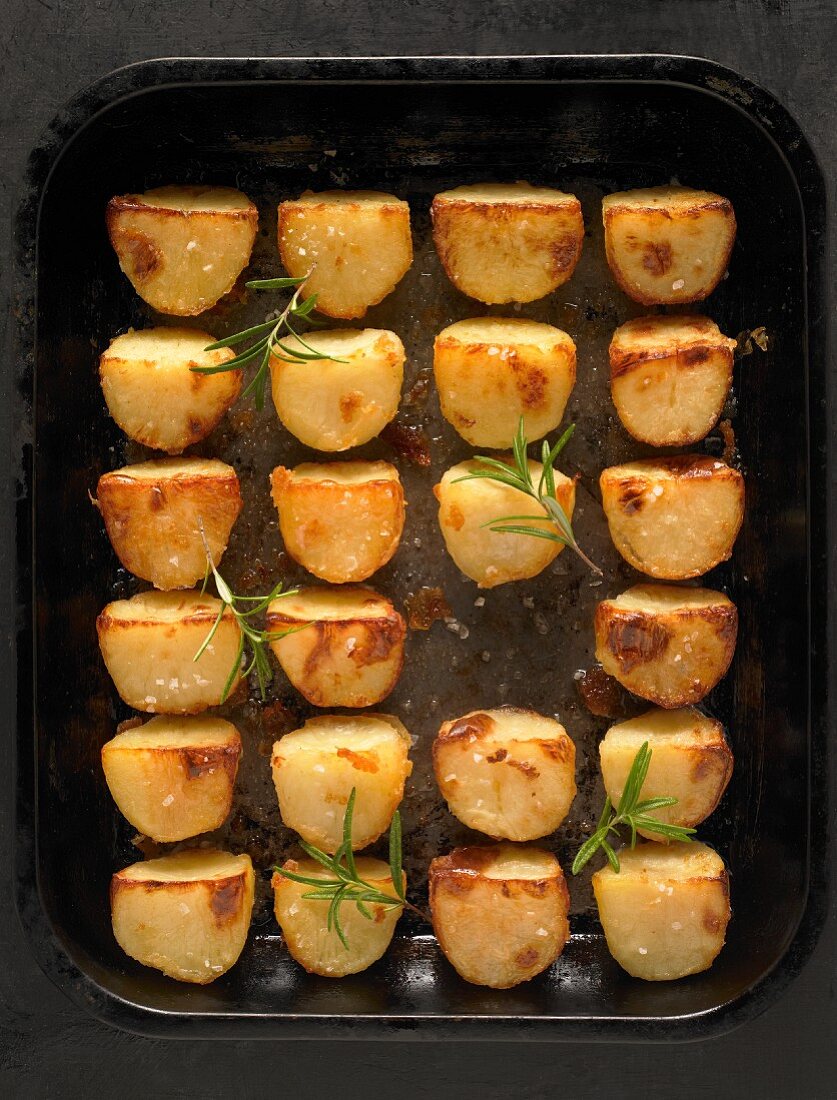 Rows of roast potatoes with rosemary on a baking tray