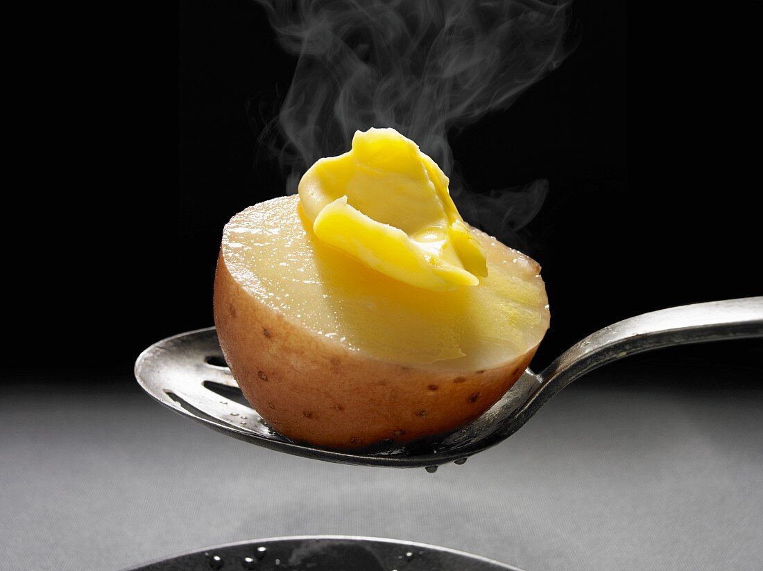 A steaming boiled potato on a spoon with melting butter