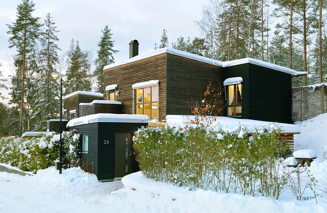 Modern, Scandinavian, flat-roofed house clad in dark wood in snowy winter landscape