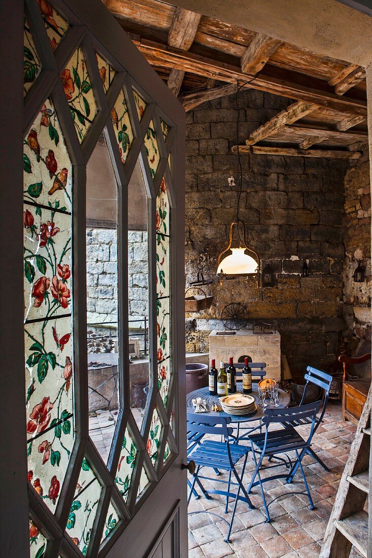 Open door with floral painted glass panels and view of sky blue garden furniture in converted stable