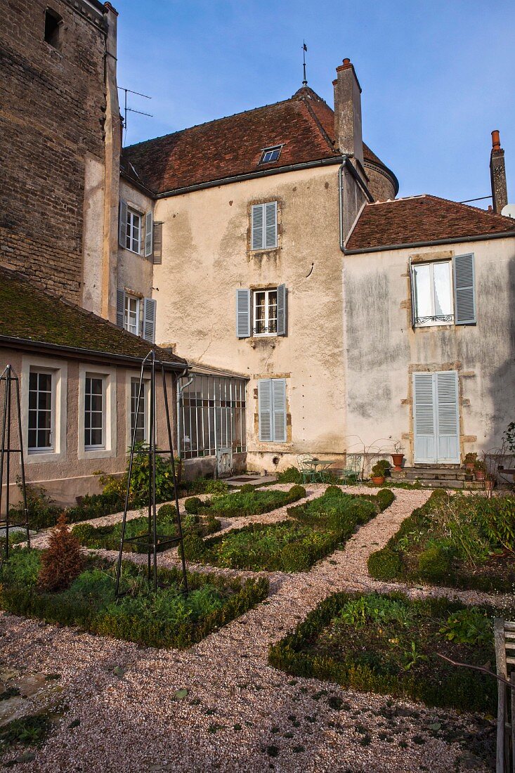 Rectangular beds amongst gravel paths in front of historical building complex in Burgundy