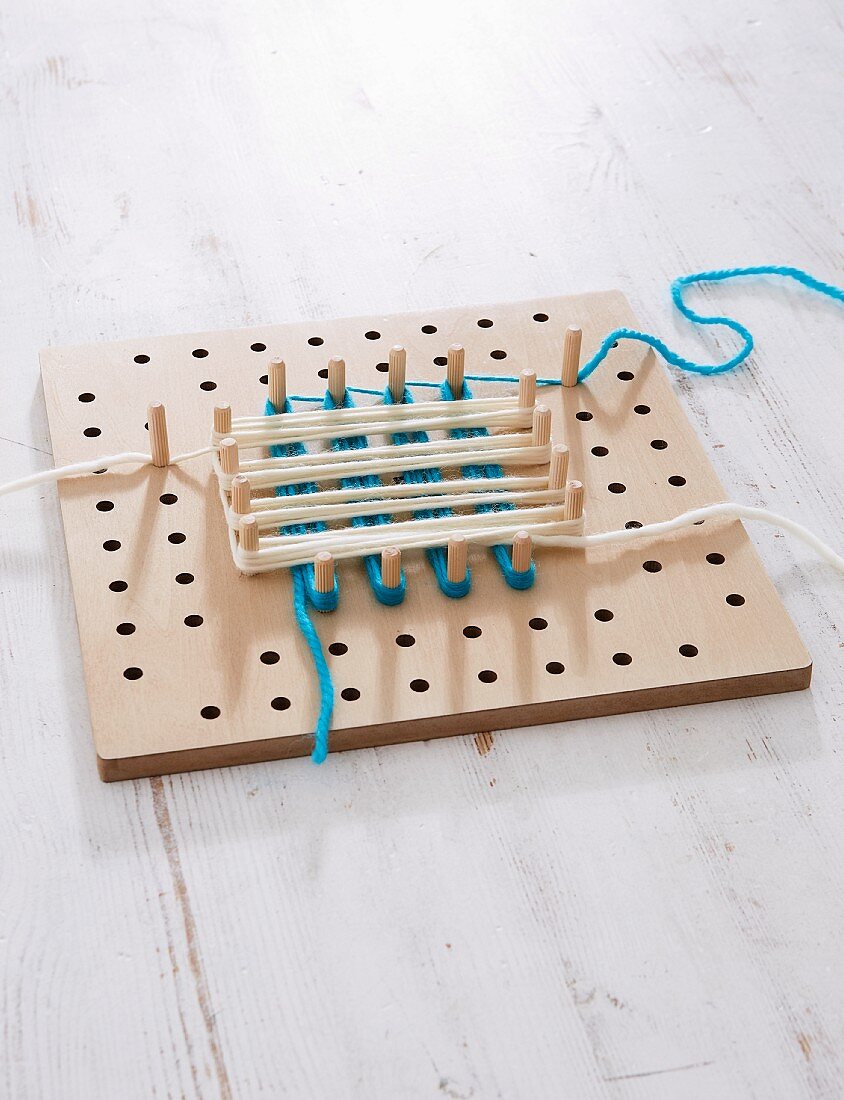 A pegboard with different coloured wool wrapped around the pegs