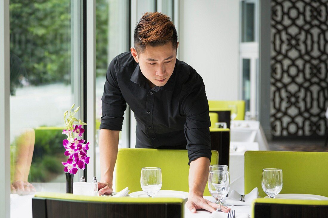 An oriental waiter placing wine glasses on tables in a restaurant