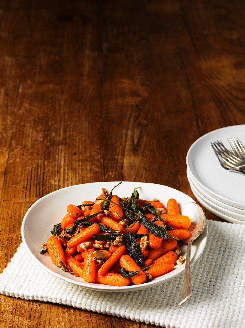 Baby carrots with sage butter and roasted walnuts on a wooden table