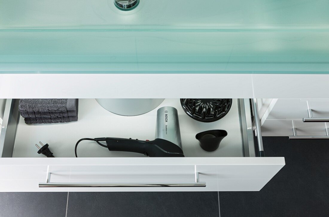Ausschnitt eines Waschtisches mit Glasplatte und halboffene Schublade, Blick auf Föhn mit Zubehör