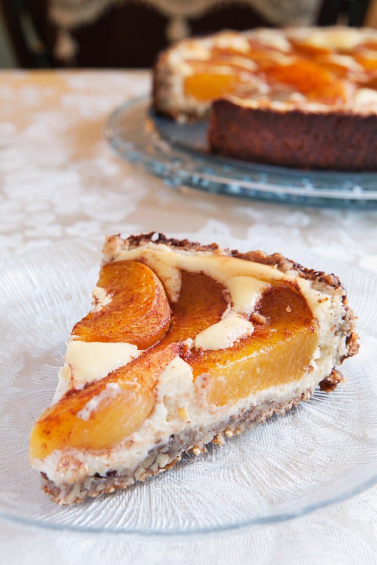 Slice of peach tart with the rest of the cake in the background