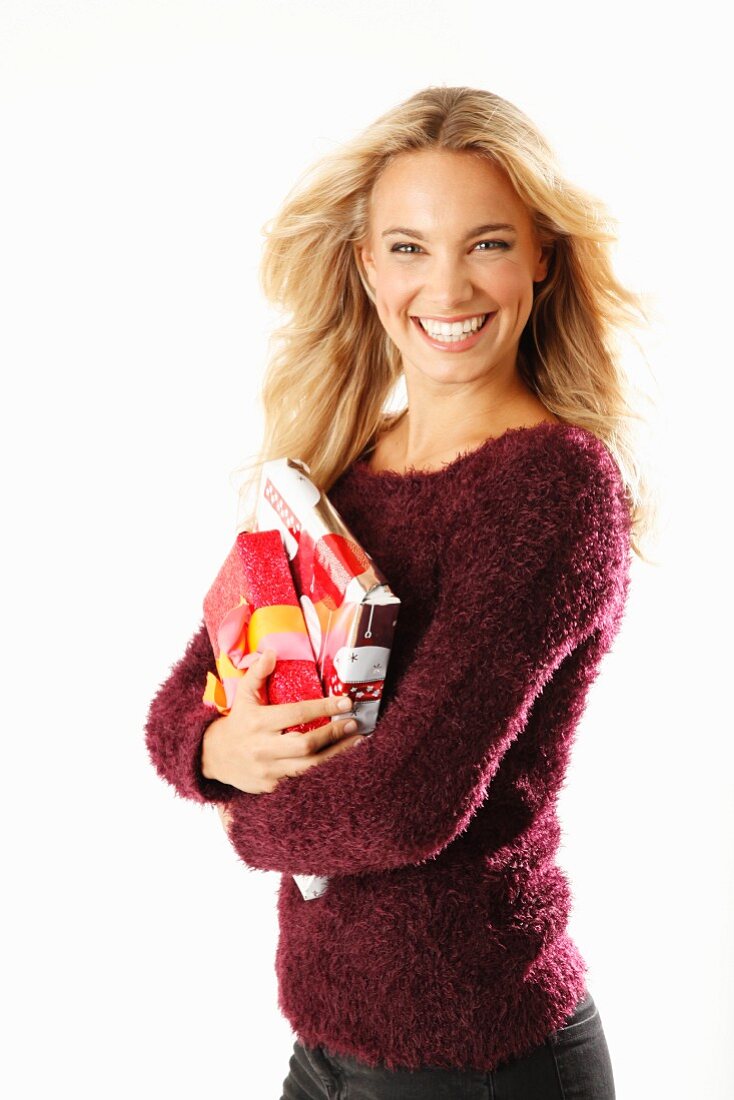 A young blonde woman holding presents and wearing a burgundy knitted jumper