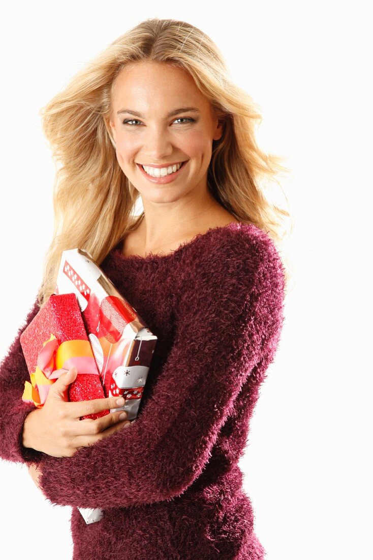 A young blonde woman holding presents and wearing a burgundy knitted jumper