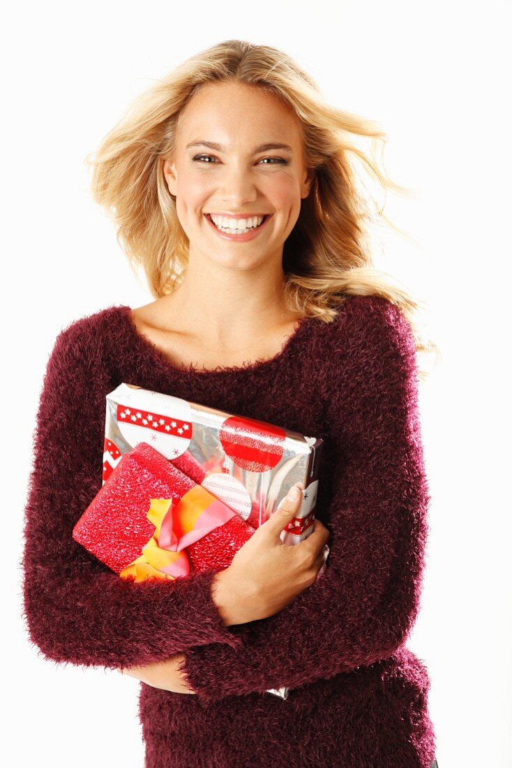 A young blonde woman holding presents and wearing a burgundy knitted jumper