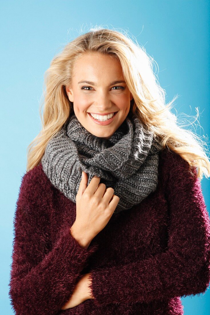 A young blonde woman wearing a burgundy knitted jumper and a grey scarf