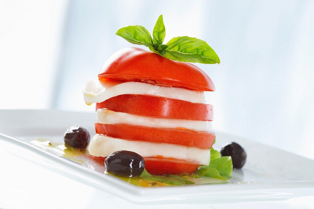 A tomato and mozzarella tower with basil and olives