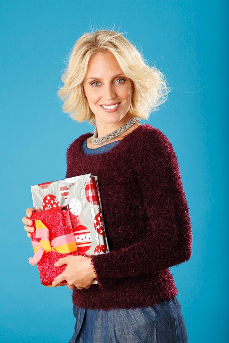 A young blonde woman holding presents and wearing a dark red jumper