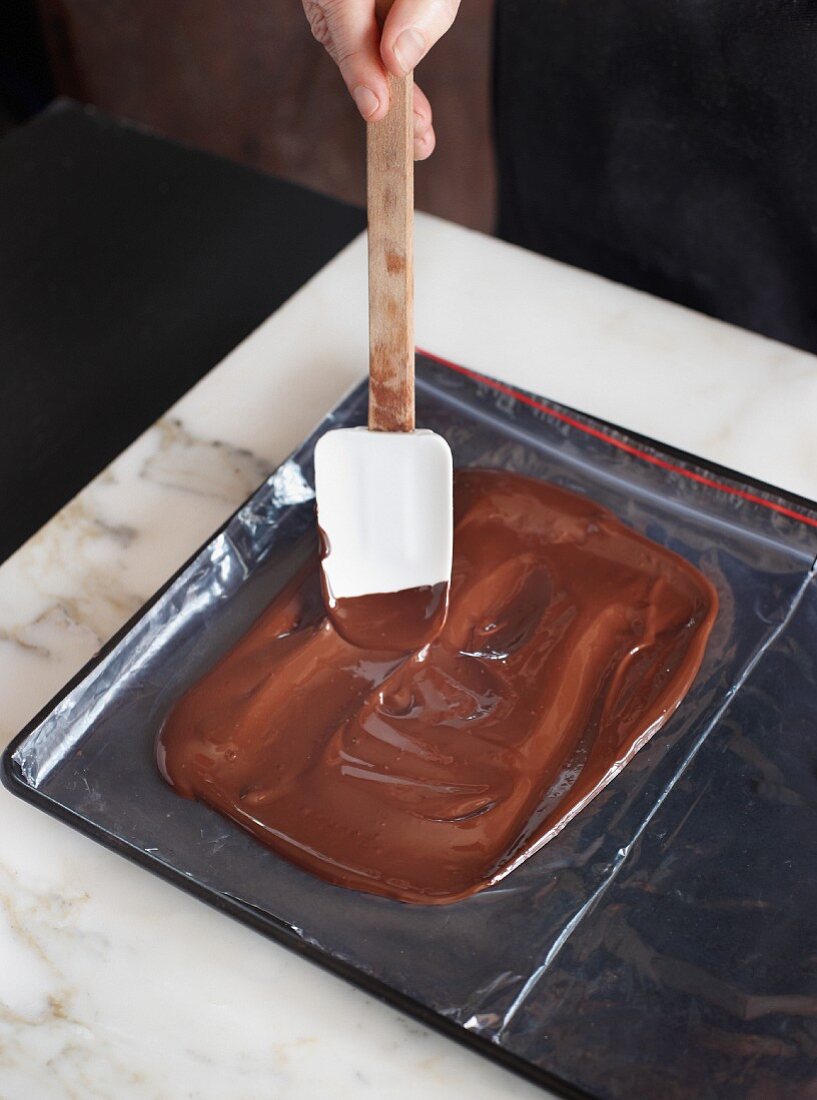 Tempered chocolate being place on cling film with a spatula