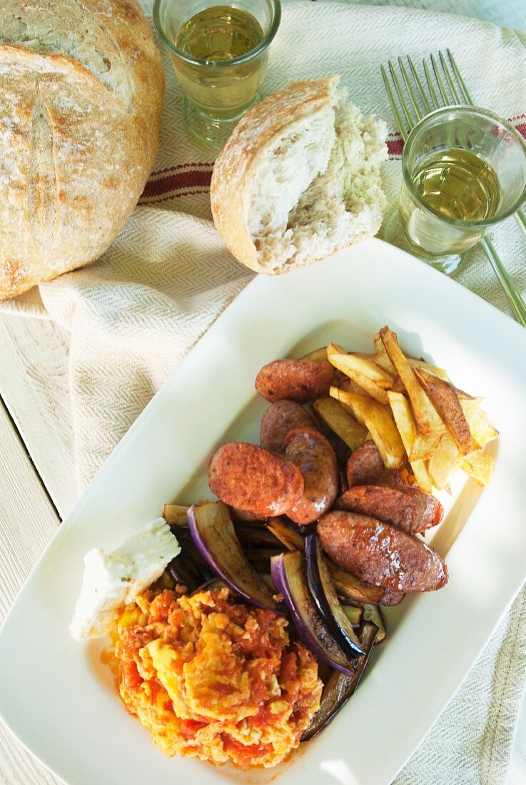 Griechische Bratwurst in Scheiben mit Röstkartoffeln, Auberginen, Feta und Tomaten-Rührei