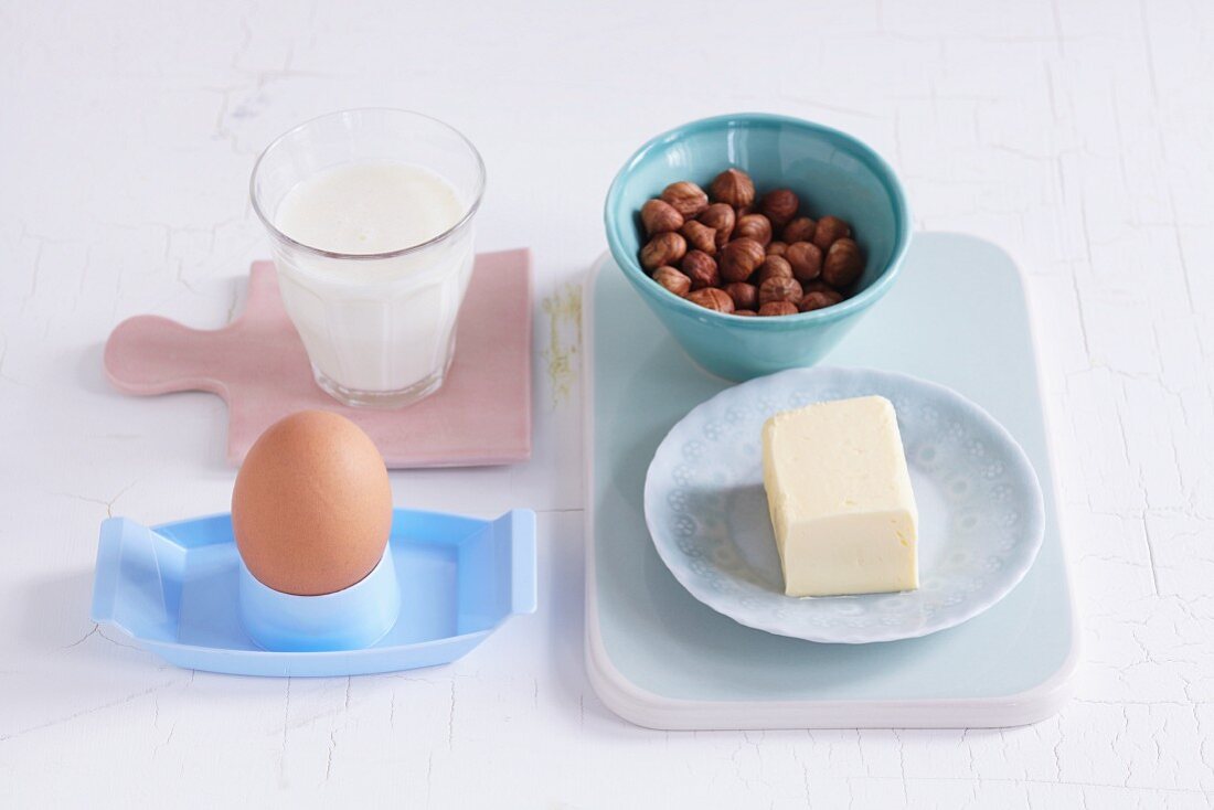 Ein Ei, ein Glas Milch, Schälchen mit Haselnüssen und ein Stück Butter