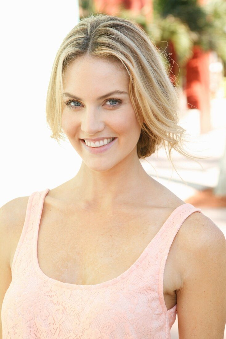 A blonde woman wearing a pink top with her hair tied back