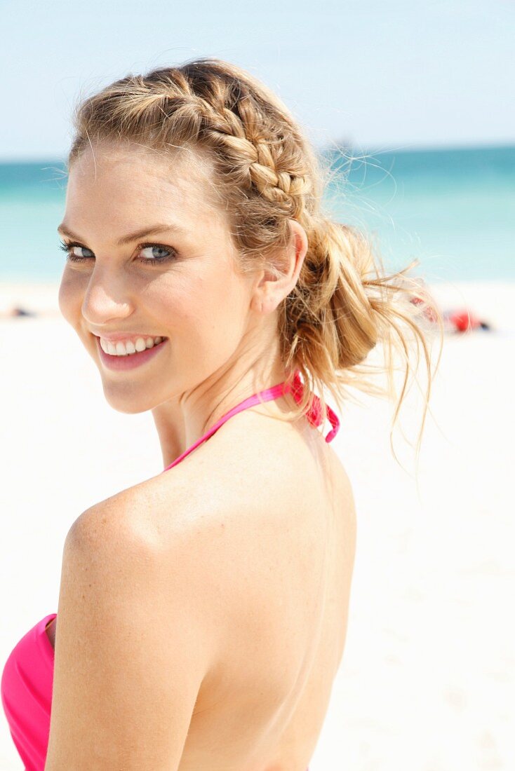 A young blonde woman on a beach wearing a pink bikini top