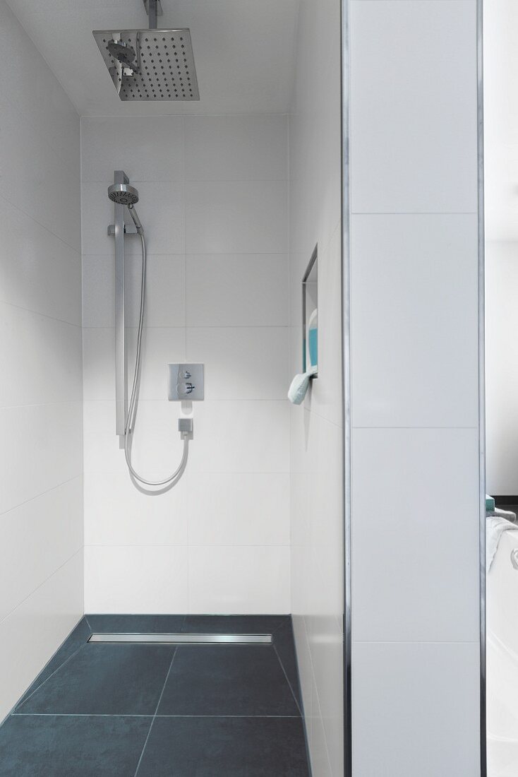 A shower head and a hand-held shower head in a modern, walk-in shower with a drain gutter