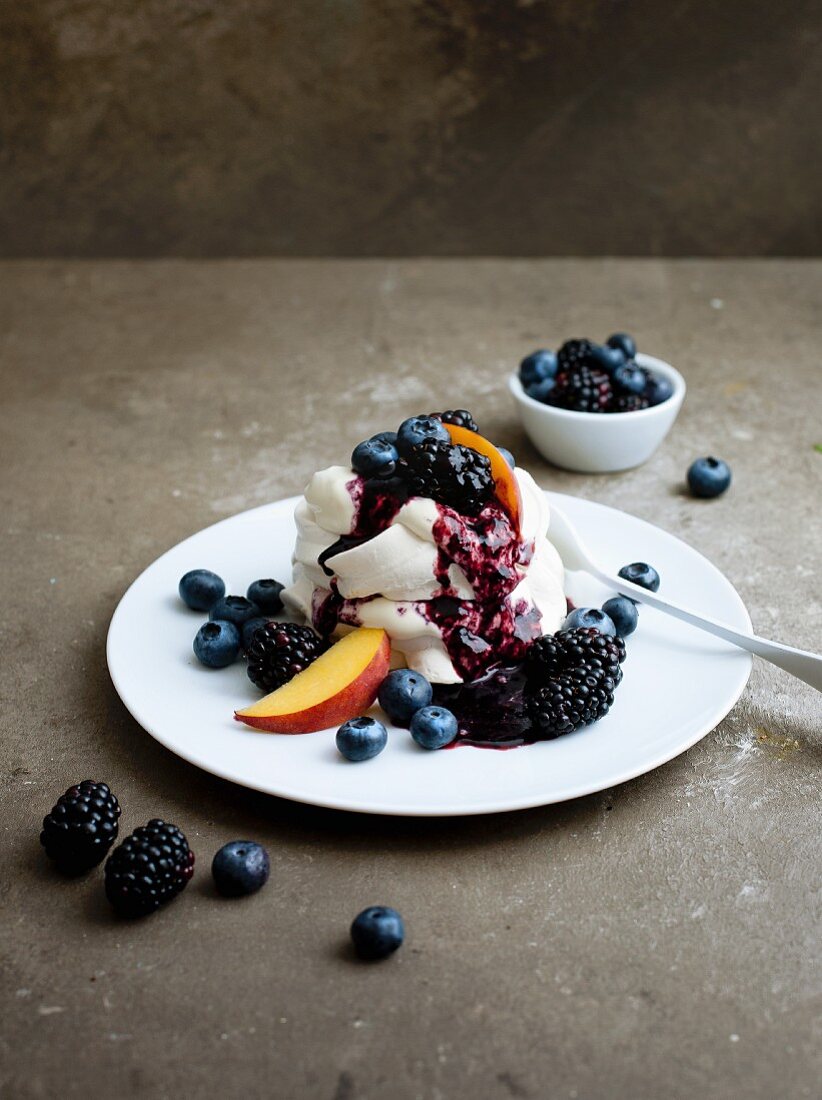 Pavlova with berry syrup, blueberries, blackberries and peaches