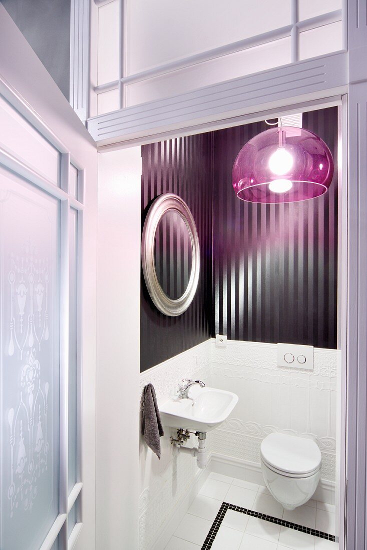 View through open door into elegant toilet with glossy, striped wallpaper and extravagant, purple, plexiglas lampshade