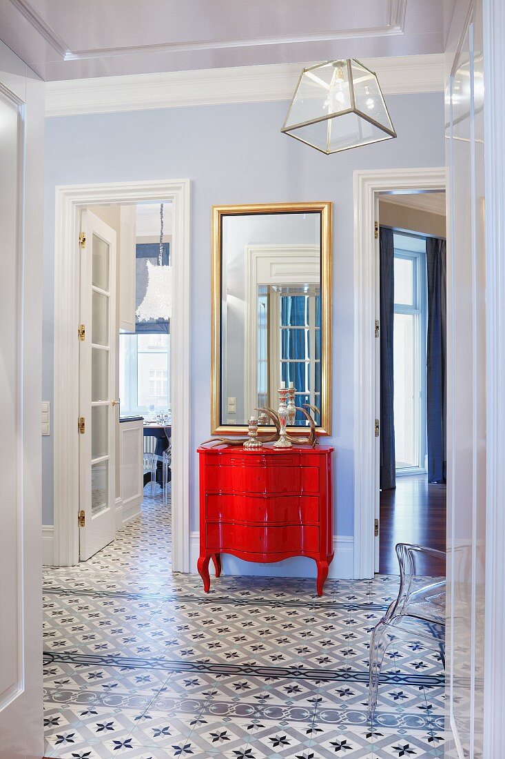Foyer with patterned tiled floor, and red, postmodern chest of drawers against wall between open interior doors