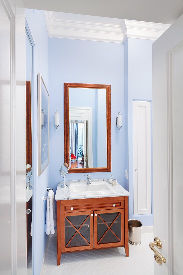 View though open door into bathroom with mahogany-coloured, wooden washstand against wall painted pale blue