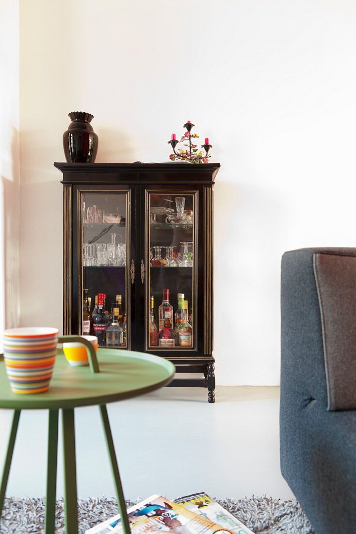 Green, retro tray table in front of antique display cabinet against wall