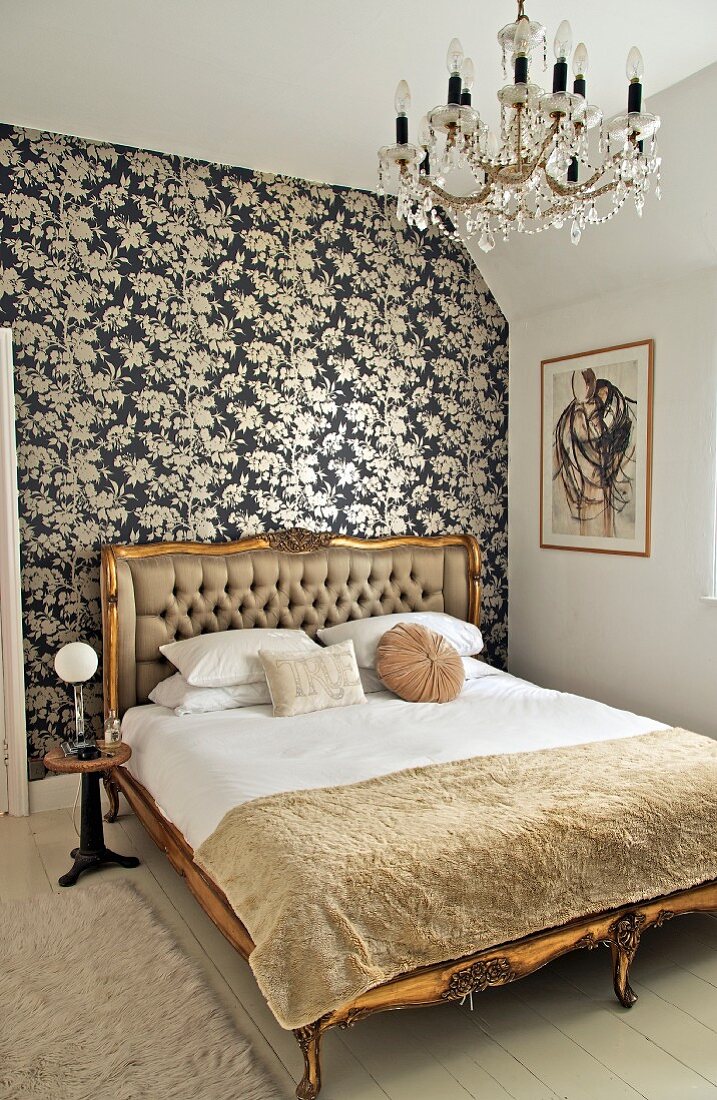 Doppelbett mit vergoldetem, antikem Holzgestell vor Wand mit schwarz-weisser Blumentapete