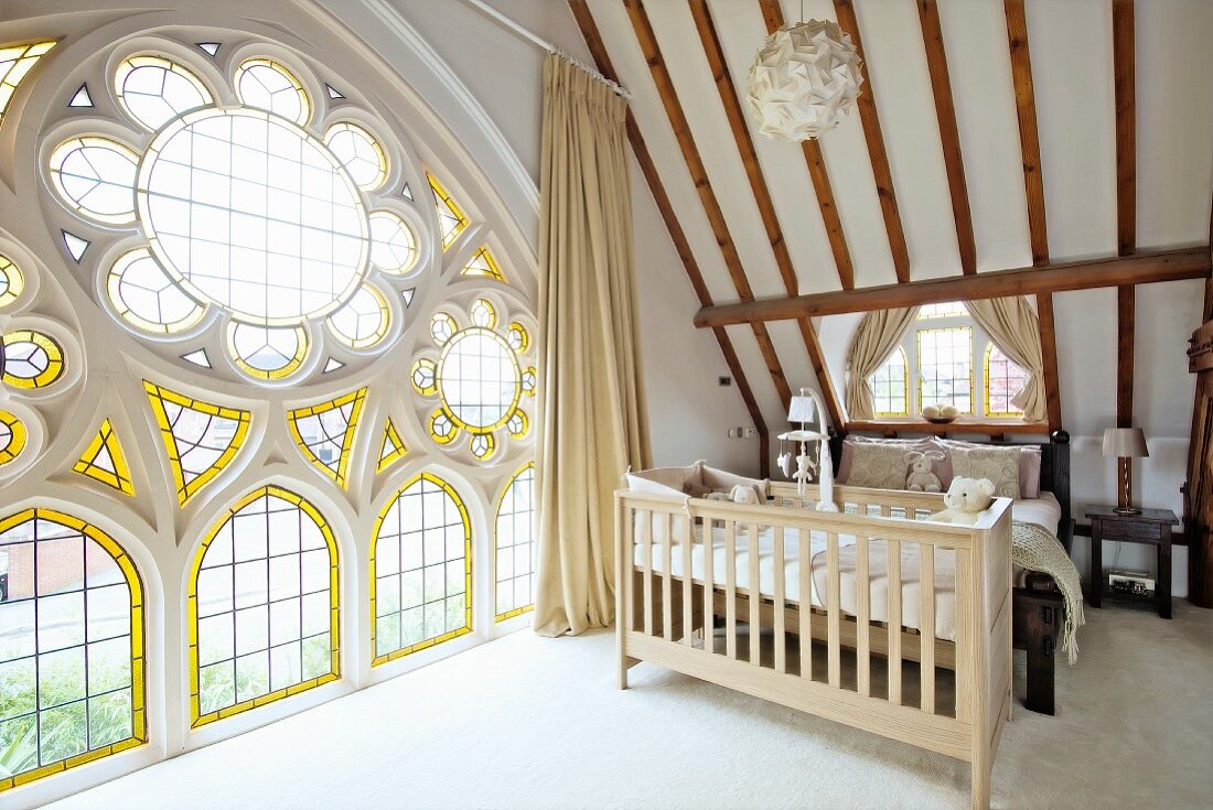 Bedroom with sloping ceiling, cot at foot of double bed and magnificent rose window with stained glass elements in converted church