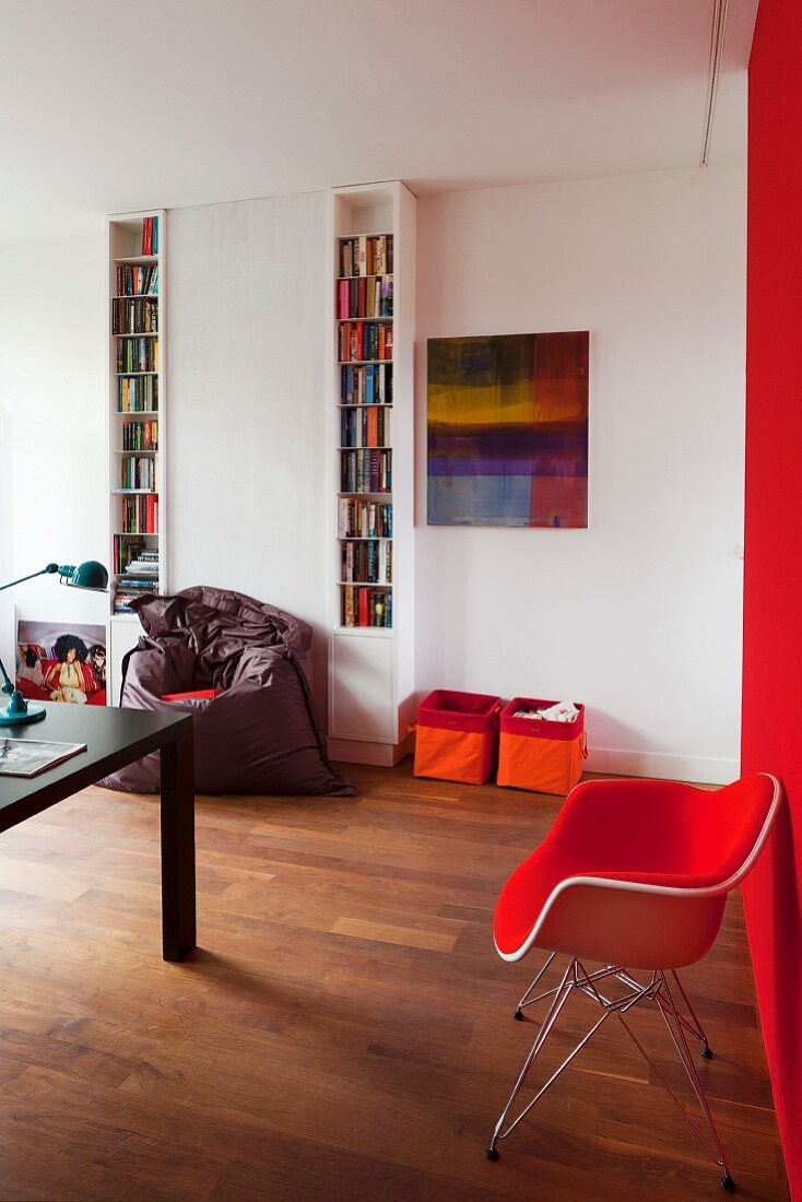 Red, classic armchair against red wall, narrow, white bookcases and fabric storage bins against wall in modern interior