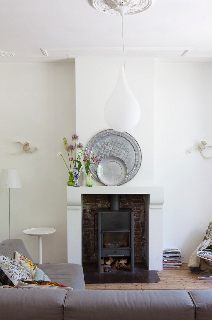 Pewter plates and wild flowers on mantelpiece; teardrop-shaped pendant lamp above sofa