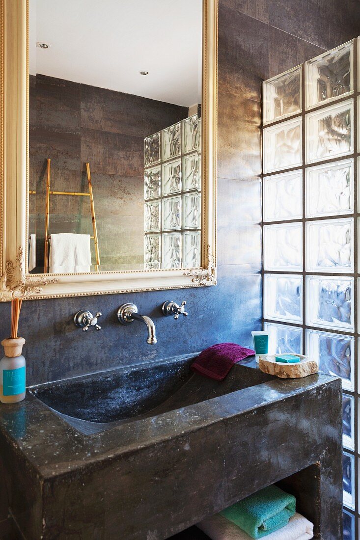 Concrete sink and mirror on dark marbled wall with glass brick partition to one side