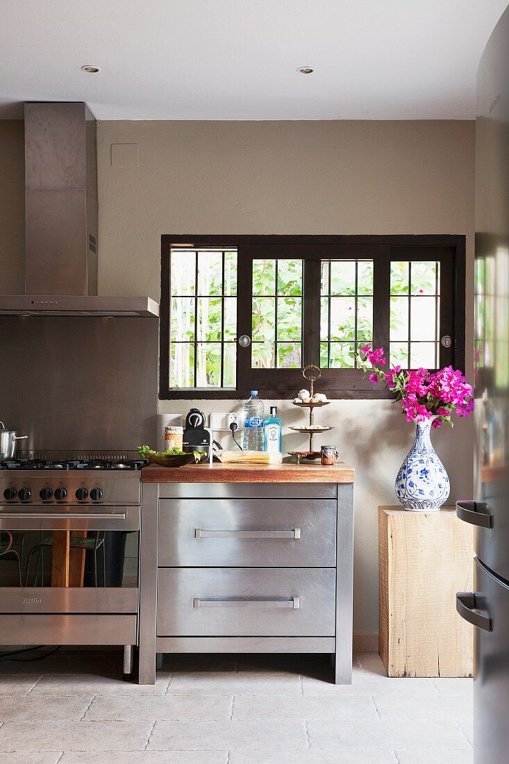 Modern stainless steel kitchen counter, stone floor and Delft vase of Bougainvillea below lattice windows