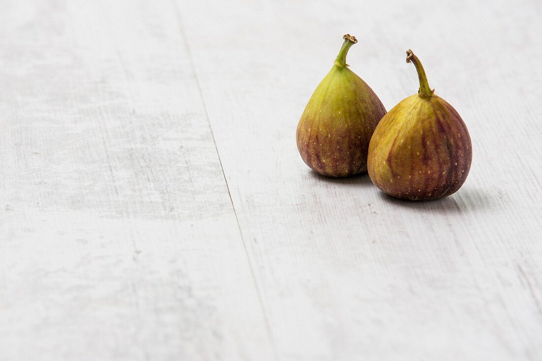 Two fresh figs on a white wooden surface