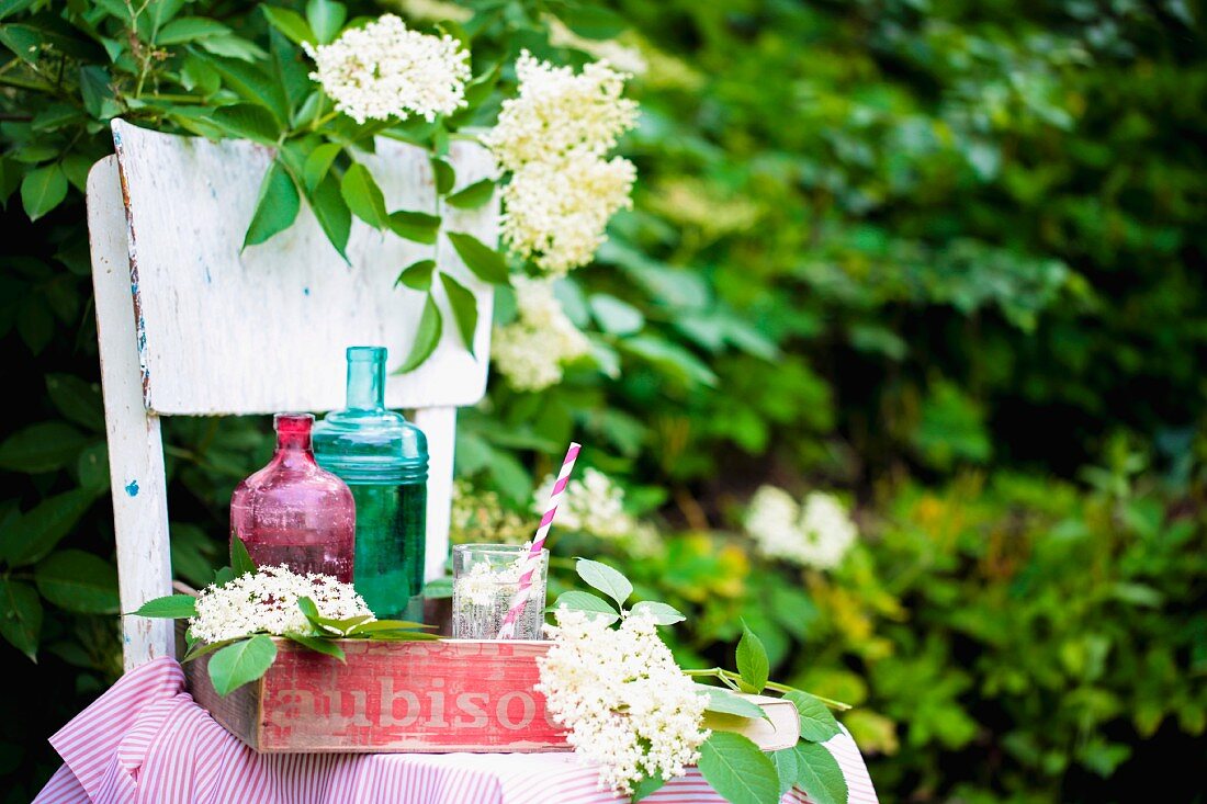 Bottles of homemade elderflower syrup on a tray on a garden chair