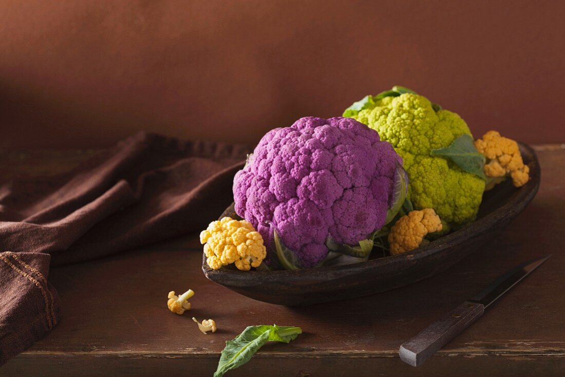 Various different coloured cauliflower in a wooden dish