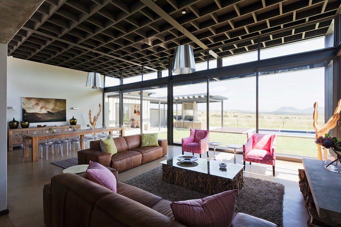 Open-plan interior with lounge area, glass wall with view of landscape and coffered-style ceiling in contemporary house