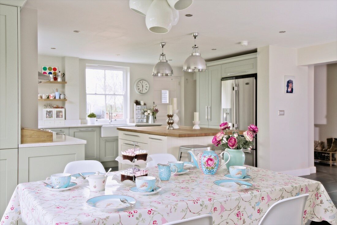 Breakfast table set with pale blue crockery in front of open-plan, country-house kitchen