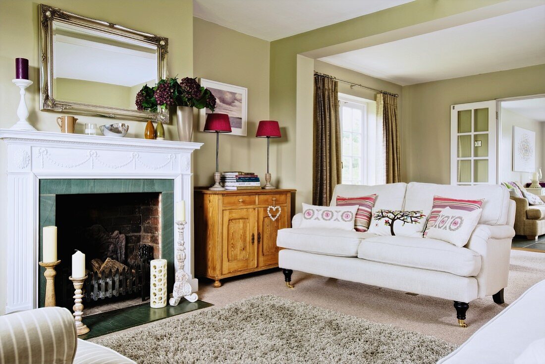 Fireplace with white surround and couch in open-plan interior with pale green walls