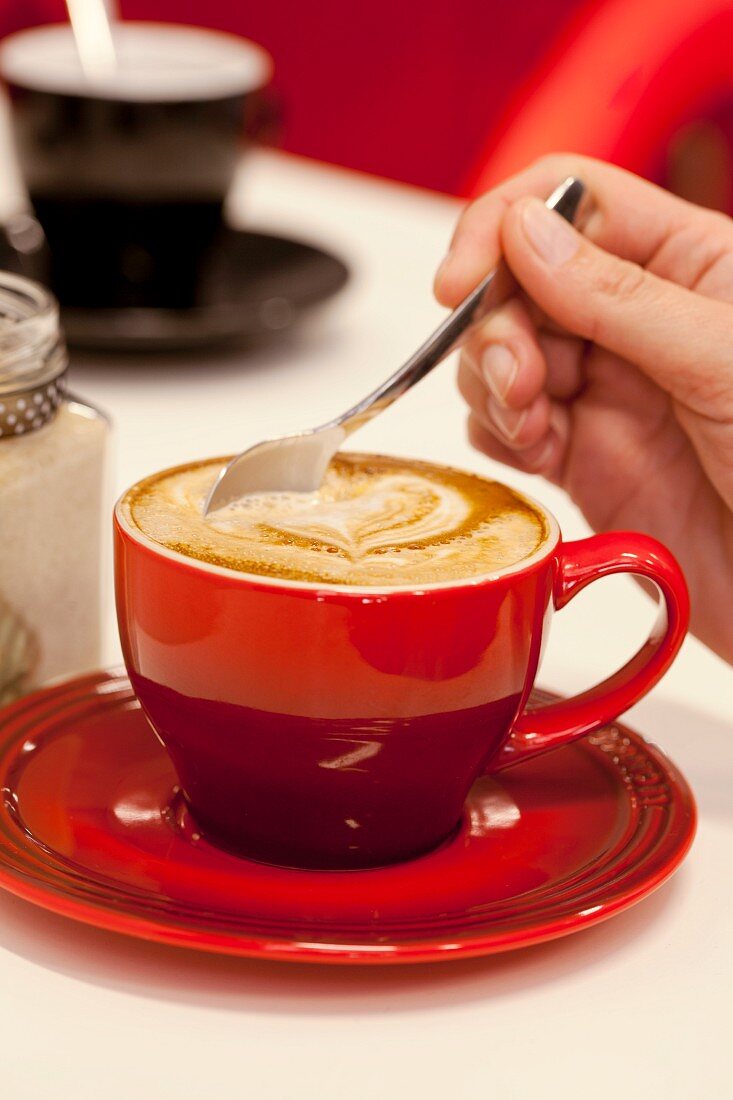Hand rührt in heißem Cappuccino mit Herzdekoration