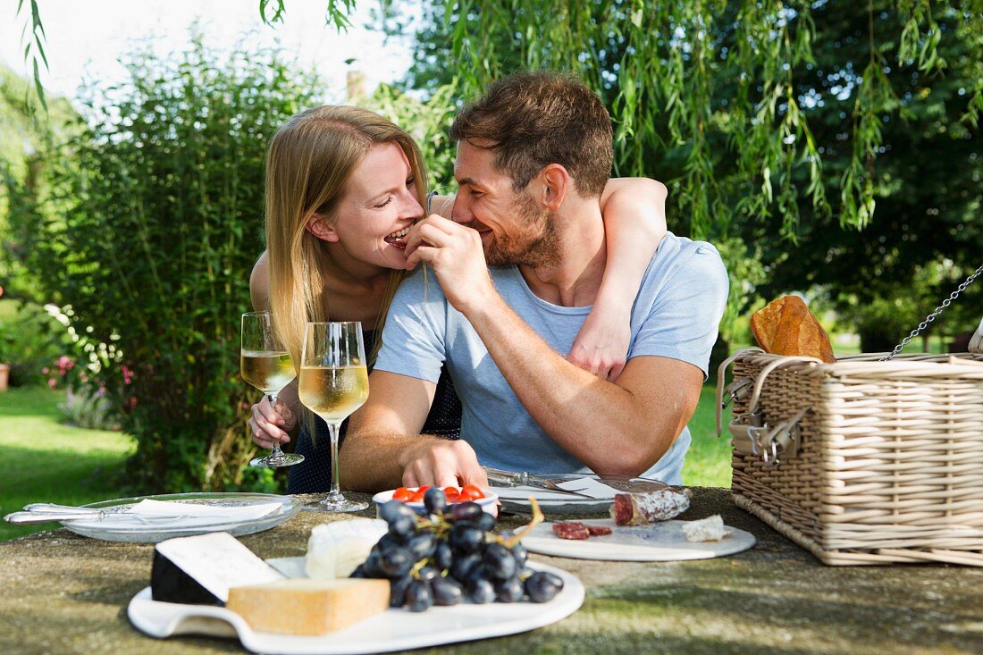 Mann füttert Freundin beim Picknicktisch im Garten