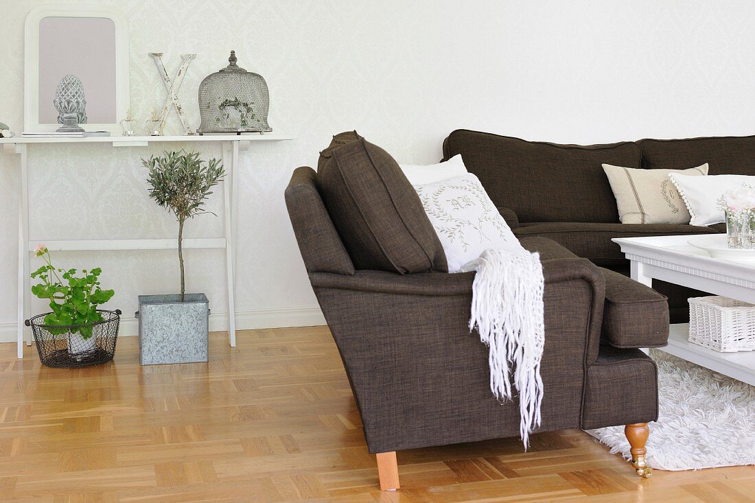 Dark sofa set around coffee table, potted plants on parquet floor and console table