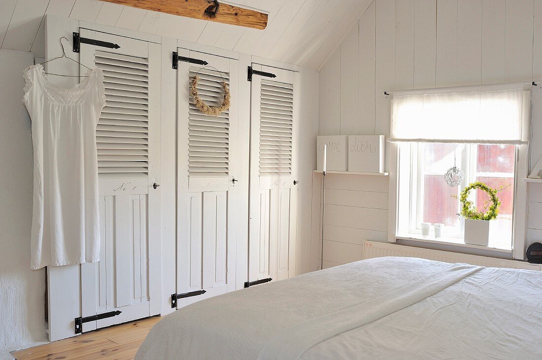Einfaches Landhausschlafzimmer mit weißem Einbauschrank, weißer Wandverkleidung und skandinavischem Vintage Flair