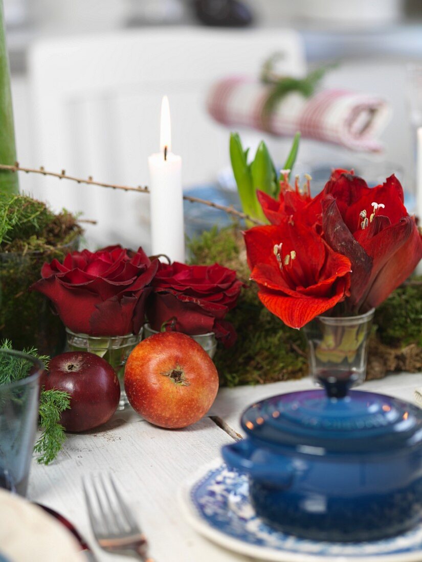 Blaues Töpfchen mit Deckel vor weihnachtlichem Tischdeko, rote Amarylisblüten und Rosen in Vase