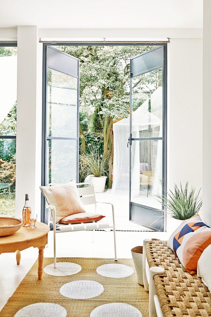 Bench with sisal seat and white chair on sisal rug with polka-dots; open door with view into garden in background