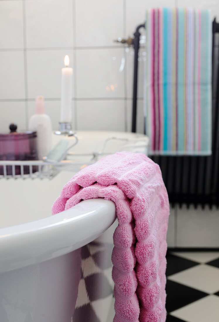 Lilac towel on free-standing bathtub and lit candle on bath rack in background