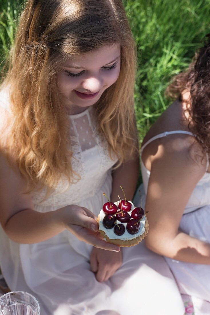 Mädchen in weißem Sommerkleid hält Tortelett mit frischen Kirschen