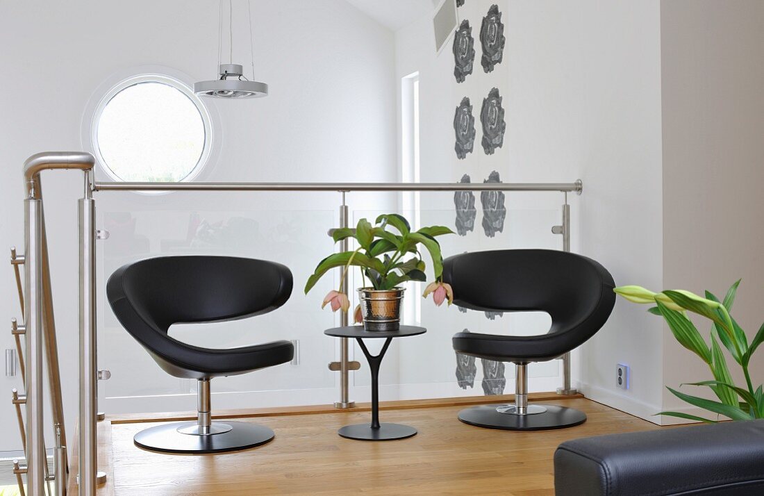 Black, designer easy chairs and side table against glass balustrade of interior staircase