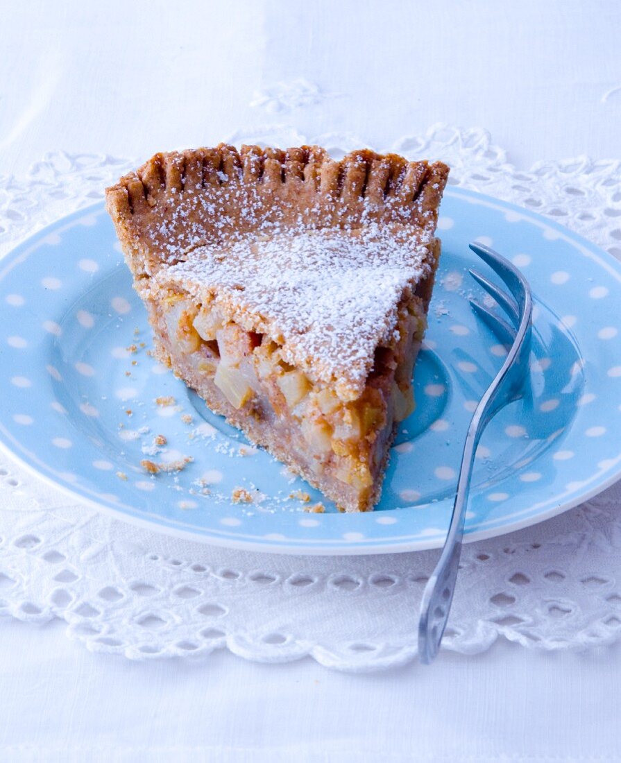 A slice of apple pie with icing sugar on a spotted plate