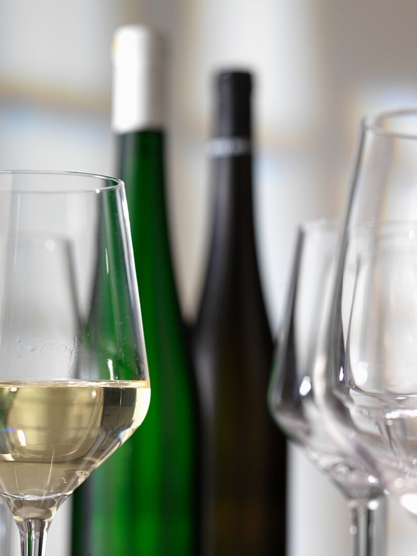 Weissweinglas, Weinflaschen und leere Gläser